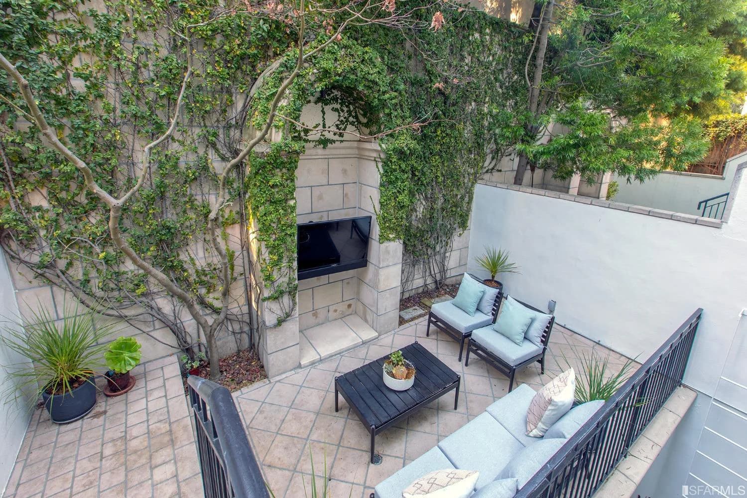 Sheltered garden terrace with seating, mature greenery, and outdoor fireplace