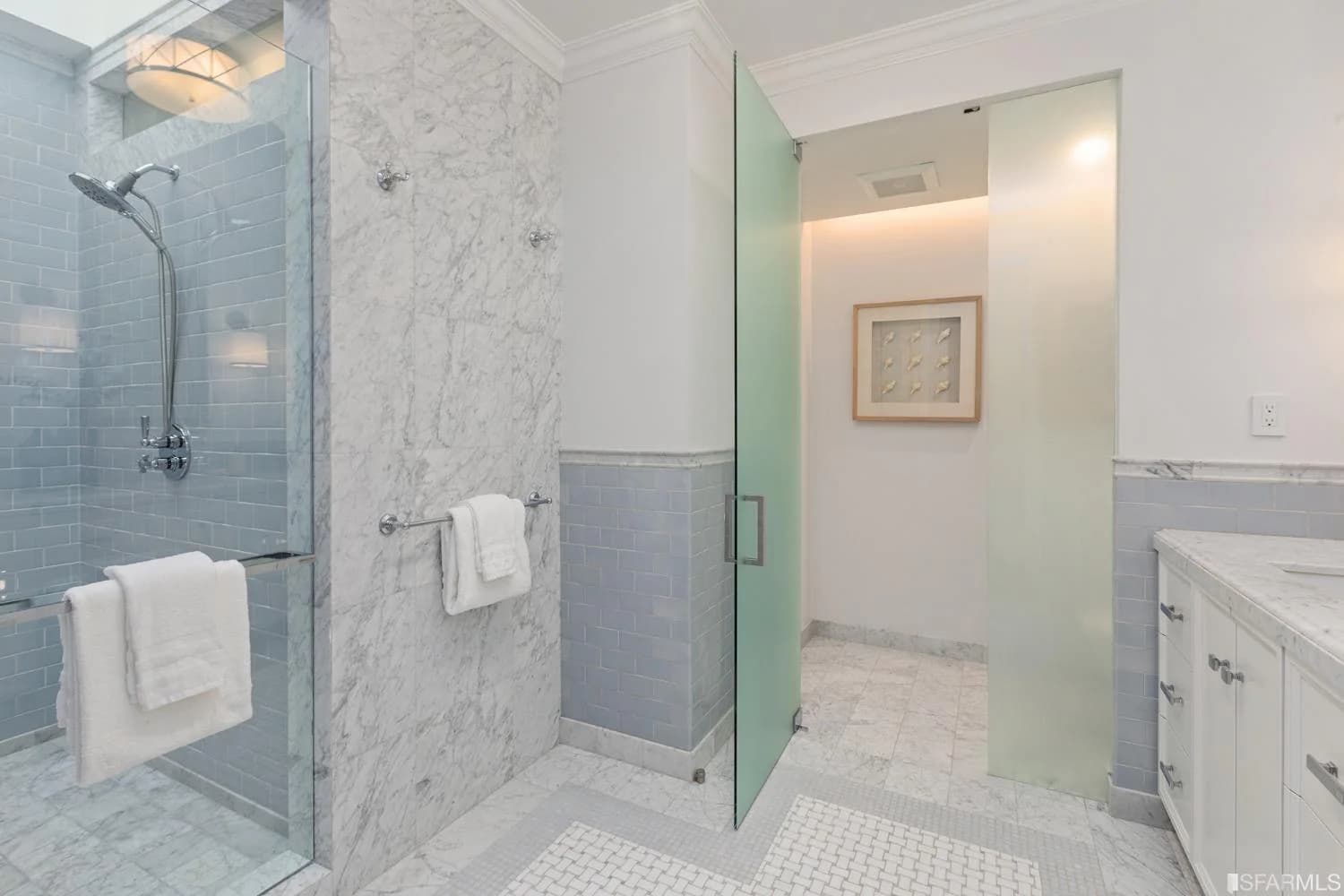 Remodeled primary bathroom with marble walls, skylight, and glass shower